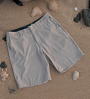 Grey hybrid swim shorts on a sandy beach with rocks on the shore.